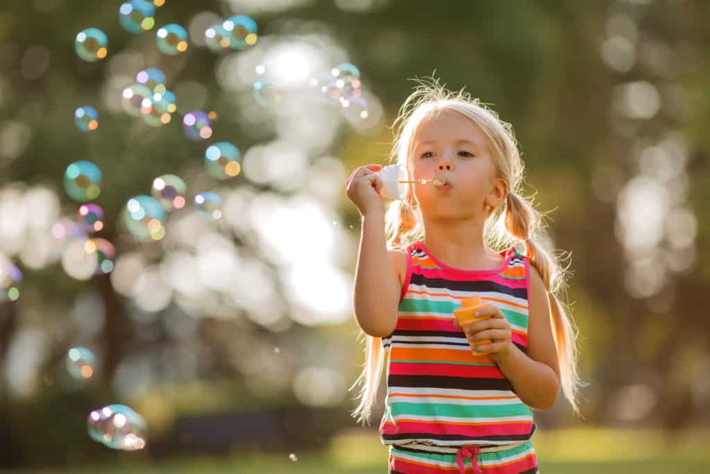 Fotografie Ploeg Benelux B.V. little blonde girl inflates soap bubbles summer walk